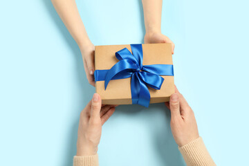 Mother giving gift box to her child on light blue background, top view