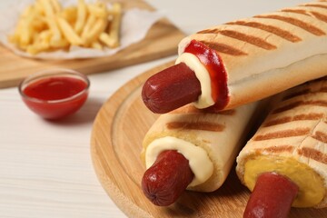 Delicious french hot dogs, fries and dip sauce on white wooden table, closeup
