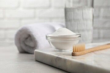 Bamboo toothbrush and glass bowl of baking soda on light table, space for text