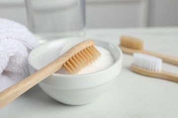 Bamboo toothbrushes, bowl of baking soda and towel on white table, closeup