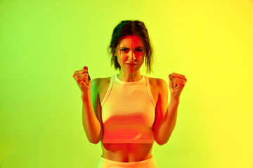 Portrait of annoyed charming girl showing fists with angry face over acid green color studio...