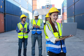 Group of multiethnic technician engineer in protective uniform standing and using computer, walkie talkie radio and tablet while.working together and controlling at container cargo site industrial