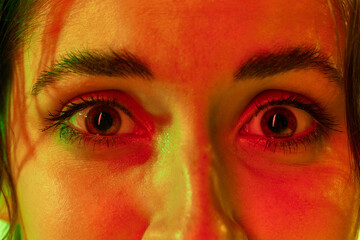 Close up portrait of young charming female face with big eyes full of fear over studio background in neon light. Dilated pupils