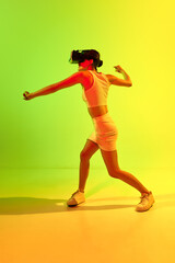 Fototapeta na wymiar Girl wearing VR headset glasses playing game over acid green and yellow background. Youth, virtual lifestyle of future. Virtual reality fight