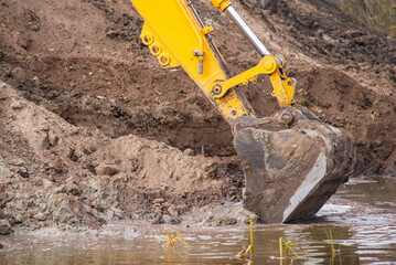 Fototapeta Close up of shovel of excavator digging artificial pond. Construction work in countryside obraz