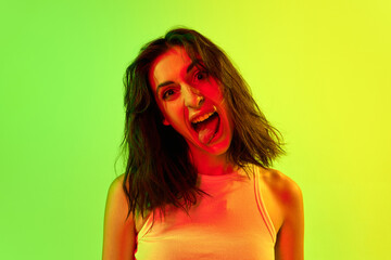 Fototapeta Portrait of adorable girl, teenage, student with short hair posing and grimacing with joyful face over yellow background in neon light. Concept of human emotions, fun obraz