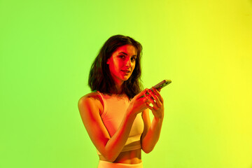 Fototapeta Young beautiful girl, student wearing stylish costume holding smartphone and looking at camera over acid yellow background. Concept of emotions, social networks obraz