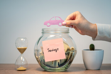 Fototapeta Woman hand holding picture of a car above the glass jar, close up. Concept of saving money and cash, financial planning, investing the vehicle and finance management obraz