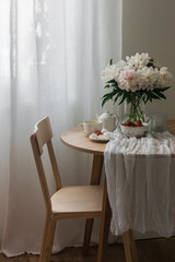 Tea party table - green tea, strawberries, meringue on a round wooden table, wooden chair, bouquet of peonies