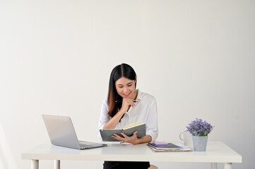 A charming young Asian businesswoman is reading or checking some details on her notebook