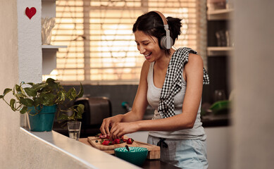 Music headphones, morning and woman cooking breakfast of healthy strawberry food at home. Kitchen, headphone and happy female person making snack with fruits while listening to audio, sound and radio