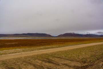 withered grass field, snow covered mountains, cloudy sky at the way from Moriri lake to Leh city, Ladakh, India