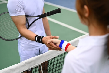Cropped shot of male and female tennis players shaking hands across net during match at court