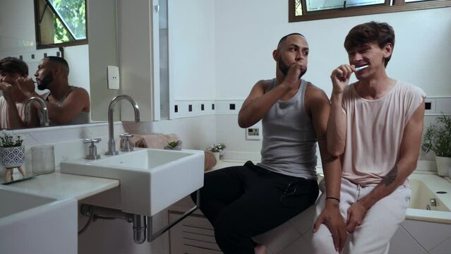 jovem casal gay inter racial latino no banheiro escovando os dentes juntos sentados na banheira no dia dos namorados