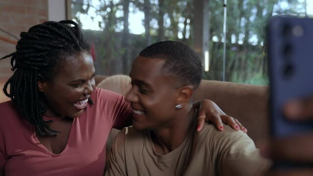 brazilian black couple sitting on living room sofa using smart phone to make video cal lon valentine's day