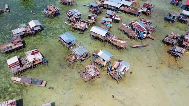 Revealing aerial shot of a boat driving in a water village of the Bajau Laut with water houses and crystal clear sea, at Omadal Semporna, Sabah, Malaysia