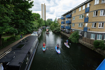 London - 05 21 2022: Boat sailing and three paddleboarders along the Grand Union Canal