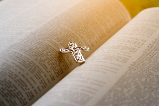 Closeup image of metal cross which places on opending bible book, soft focus, concept for religious lifestyle of christian people around the world.