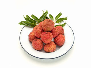 Fresh ripe lychees with green leaves on a white plate on a white background.