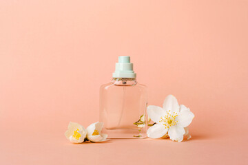 Fototapeta na wymiar Perfume glass bottle and white jasmine flowers on peachy background. Closeup