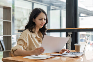 businesswoman using calculator and laptop to calculate company financial result On wooden table in office and business background, tax, accounting, statistics and analytical research