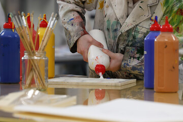 An artist or visual art student in the artroom squirting or pouring acrylic paint from a white...