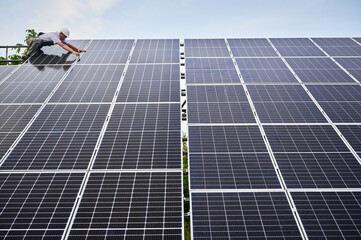 Worker installing solar panel. Renewable and ecological energy. Idea of environment safe. Modern technology and innovation. European man wearing workwear and helmet. Bottom view. Sunny daytime