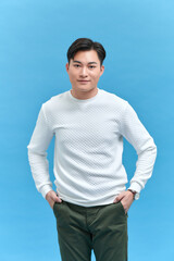 portrait of smiling young handsome Asian man standing with one hand in pocket