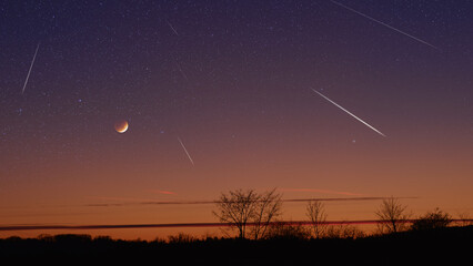 Silhouette of a countryside with Milky Way starry skies, meteor shower and crescent Moon.