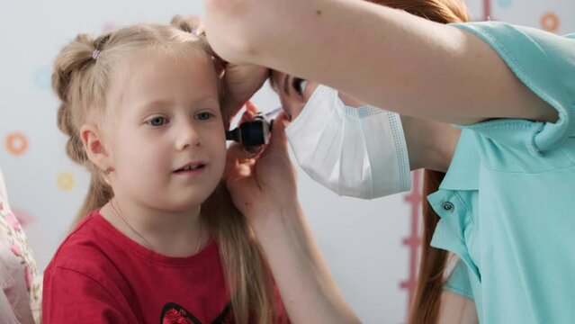 A pediatrician in a hospital checks the ear of a little girl.