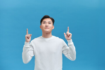 Smiling young Asian man pointing his index finger up to empty space