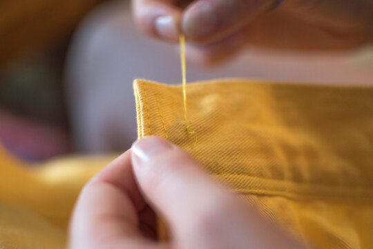 hands sewing on a button of a yellow jacket