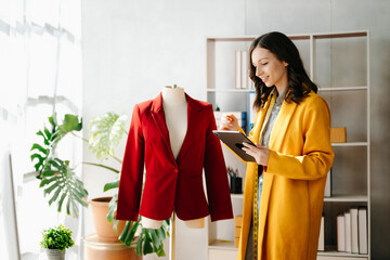 Fashion designer woman talking smart phone and using laptop with digital tablet computer in modern studio the clothes hanging on the racks .