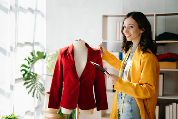 Fashion designer woman talking smart phone and using laptop with digital tablet computer in modern studio the clothes hanging on the racks .