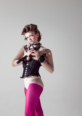 High fashion. Portrait of young extravagant girl in black corset and pink tights against grey studio background