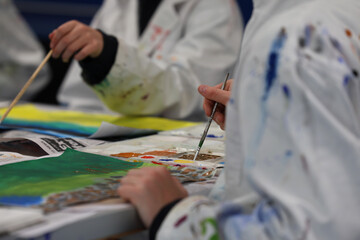 Visual art students wearing stained white smocks or aprons mixing paints on a paint palette for a...