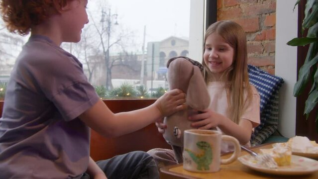 A children's date in a cafe. Stock footage. A children's holiday where a boy gives a girl a soft toy and they drink hot cocoa.