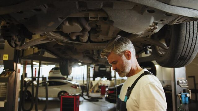 Car diagnostics. Auto service. Skillful professional middle age master performs maintenance, oil change, computer diagnostics, replacement of auto parts, repair of brake system. Auto mechanic.
