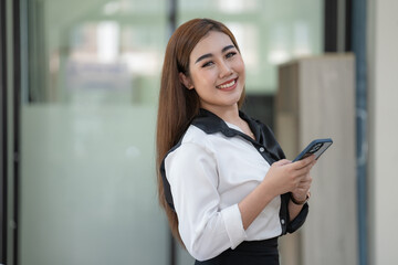 Asian businesswoman holding a mobile phone and looking at a camera.