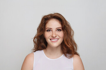 Fototapeta premium Portrait of cheerful redhead woman with healthy wavy ginger hair and fresh clear skin smiling on grey background