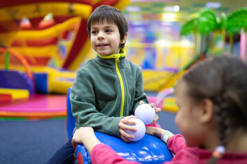 Little smiling boy and girl having fun on kids’ slide in amusement center for kids