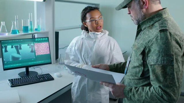 Medium shot of military man holding top secret folder listening to female scientist showing photo of cells in computer and talking about research results