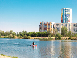 Fototapeta na wymiar man rowing on paddle surf board SUP in the lake in the city among the houses