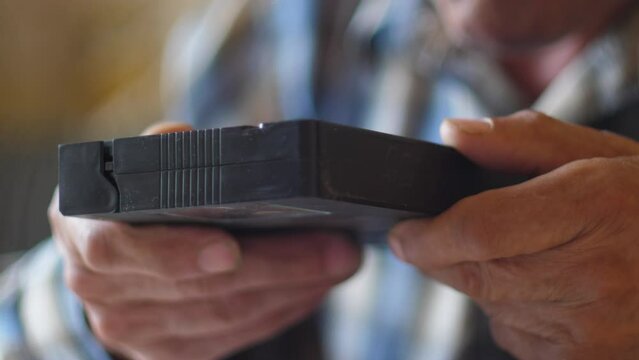 close-up of a pensioner blowing dust off a video cassette, old home archival videos on a video cassette. a reminder of the past
