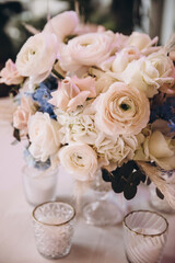 Wedding. Decor. Floristics. The festive table is decorated with a composition of pink and blue flowers with leaves of greenery. There are candles, glasses and plates on the table