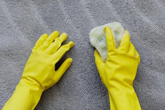 cleaning concept - top view of hands in yellow rubber gloves cleaning carpet with sponge and foam