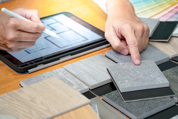 Architect hand choosing and pointing stone and wood material samples while working with digital...