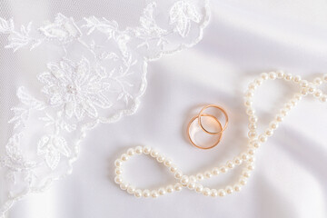 Beautiful wedding background. Two gold wedding rings on white satin with a richly embroidered bridal veil and pearl beads. postcard, cover.