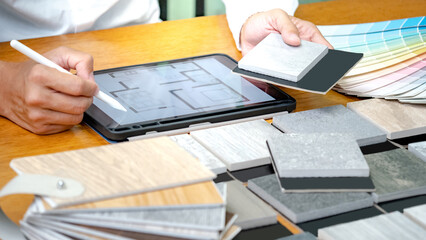 Architect hand choosing and picking stone and wood material samples while drawing on a digital...