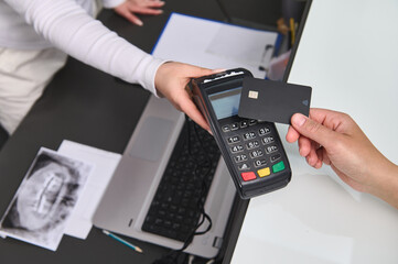 Top view customer hand holding a black mockup credit card above a POS terminal, making wireless or cashless payment using NFC technology. Close-up. Copy advertising space. People, business and finance